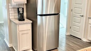 A kitchen with white cabinetry, a stainless steel refrigerator, and a coffee maker on the countertop.