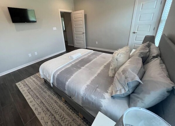 A bedroom with a bed, a small rug, a TV on the wall, and a door leading to another room. - Beautiful 3R-2B Home in Quiet Community (Edinburg)