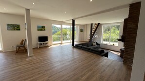 A spacious living area with a large sofa, a television on a stand, and a staircase leading to a balcony. - Traumaussicht, Traumwanderungen, Viel zu Entdecken und Richtig Viel Platz!! (Daun)