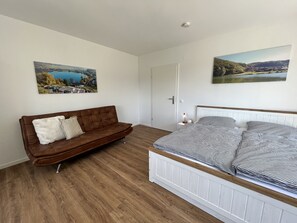 A bedroom with a brown leather sofa, a bed with striped bedding, and two landscape paintings on the walls.