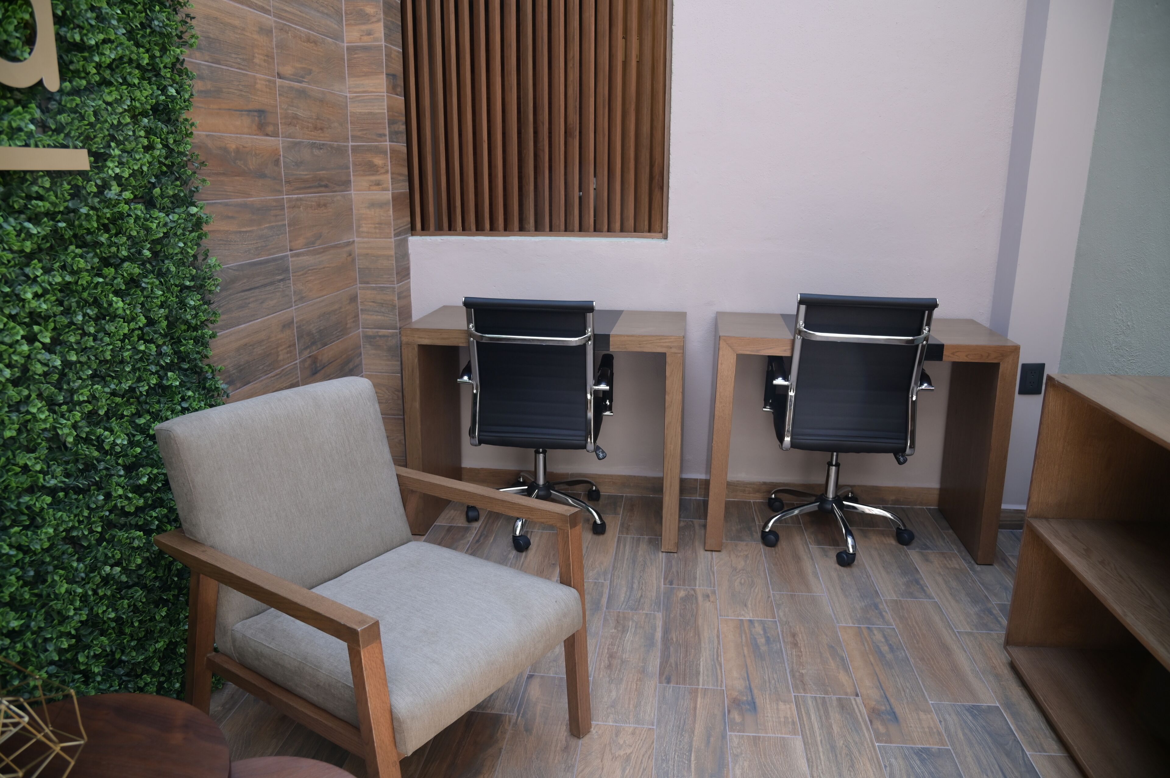 A modern office space with two black office chairs, a wooden desk, and a cushioned chair.