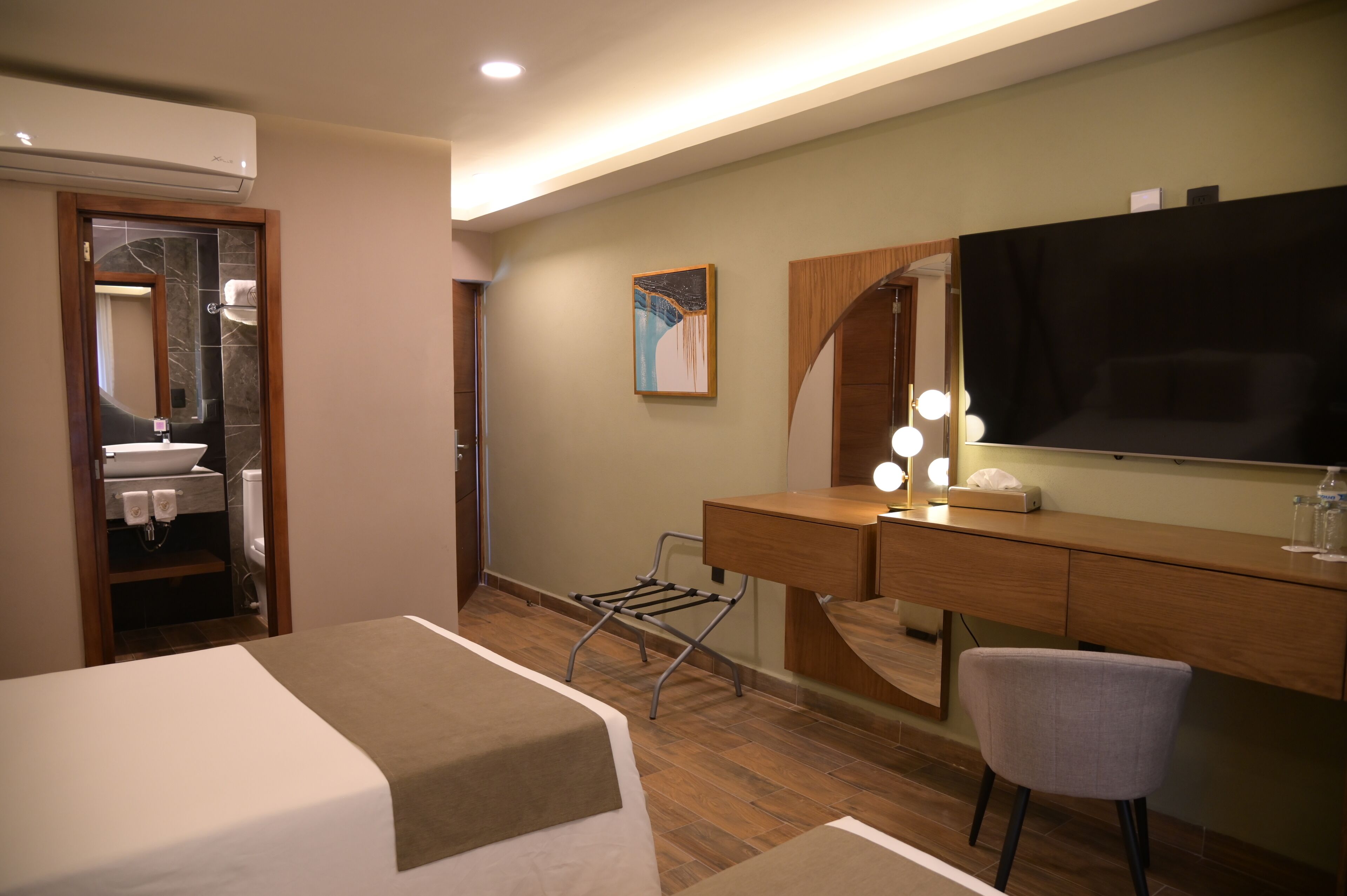 Habitación de hotel con cama, tocador con espejo, escritorio y silla, y televisión.