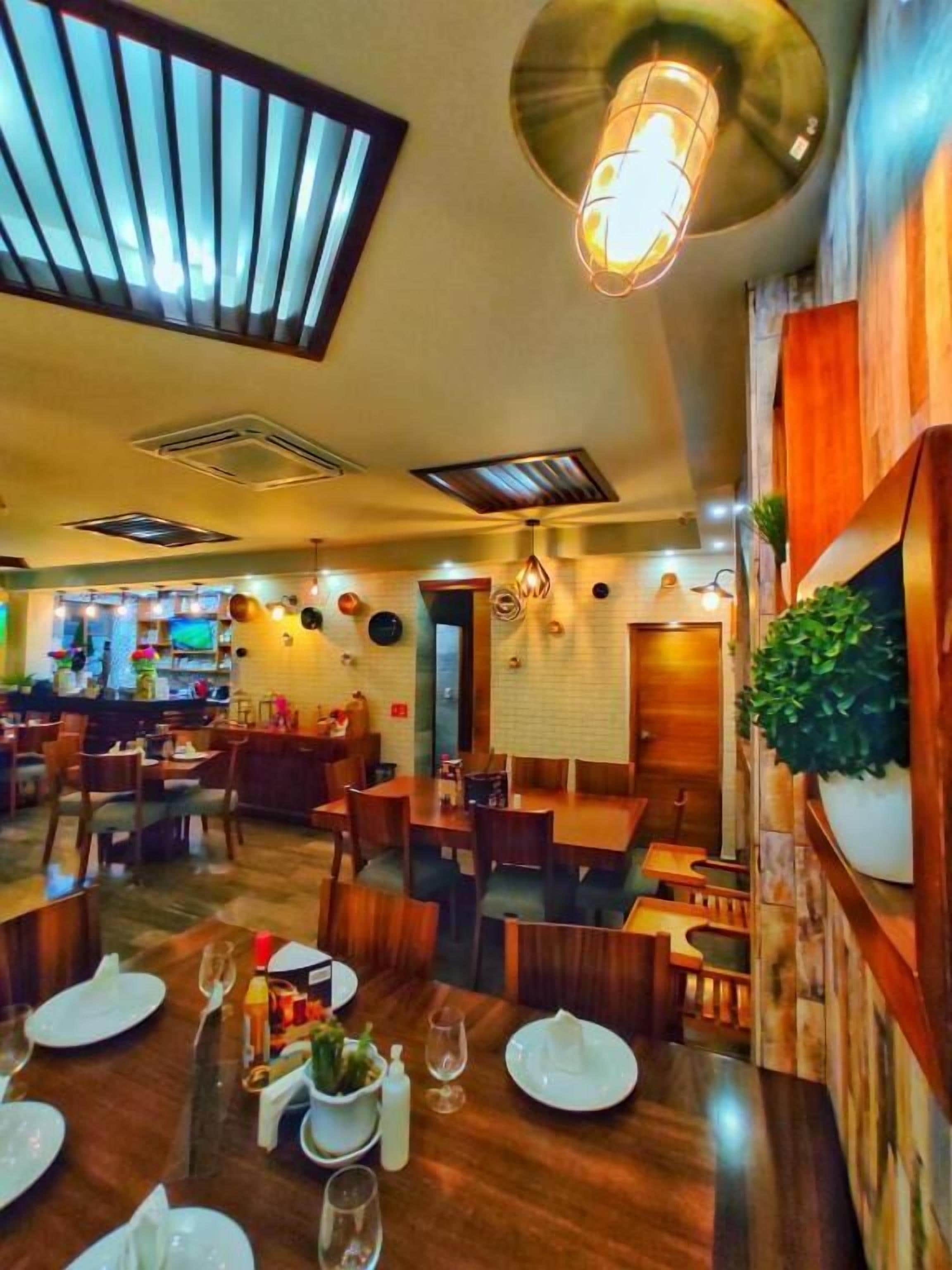 Un restaurante con mesas y sillas de madera, una zona de bar y vistas a la cocina.