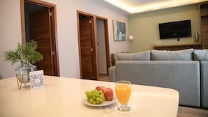 Una sala de estar moderna con un sofá gris, un televisor montado en la pared y una mesa de comedor con un código QR, fruta y un vaso de jugo de naranja.
