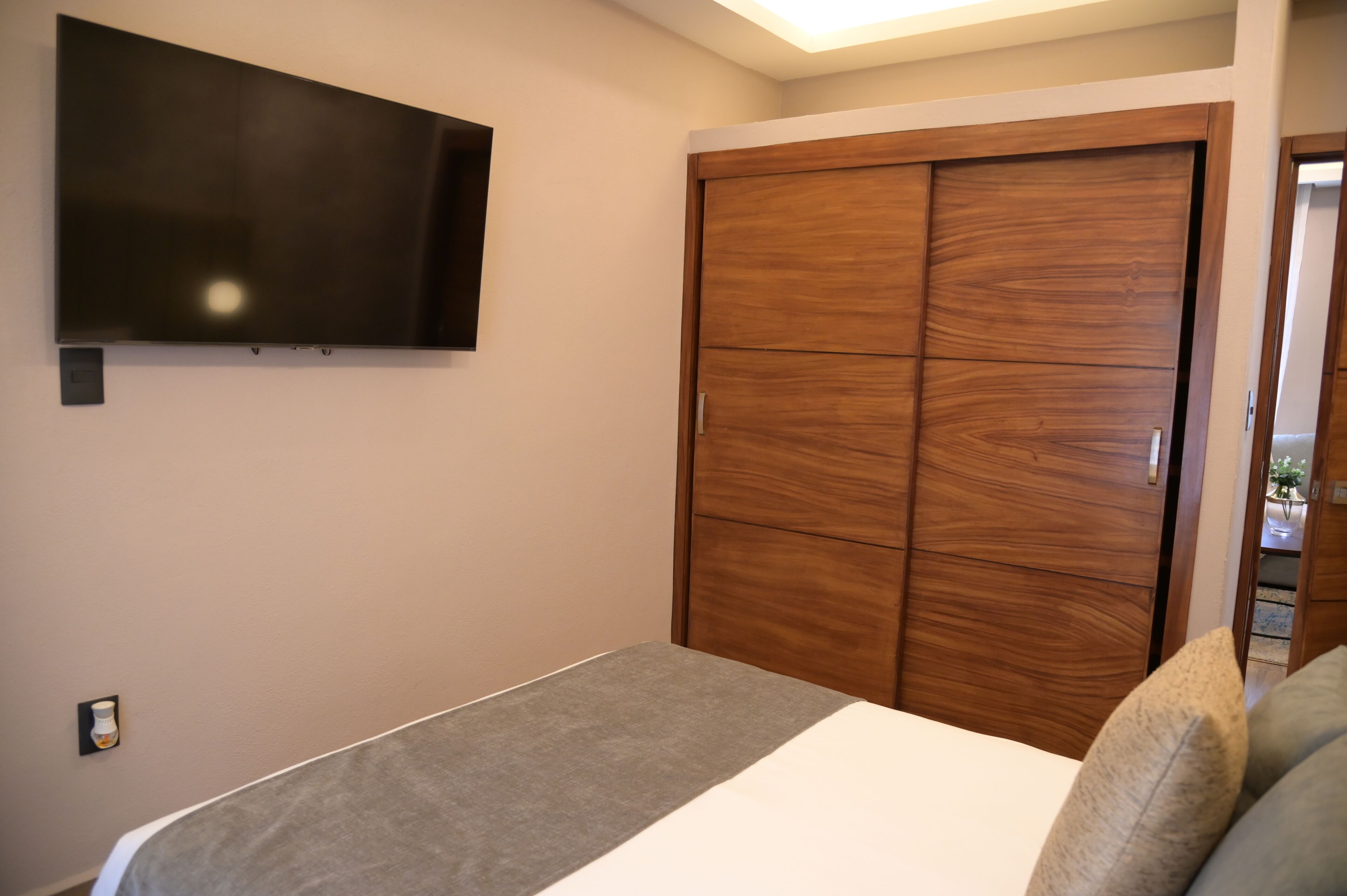 Un dormitorio con una cama, un televisor montado en la pared y un armario de madera.