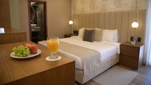 Habitación de hotel con cama, mesitas de noche, lámpara de noche, un plato de fruta y un vaso de jugo de naranja.
