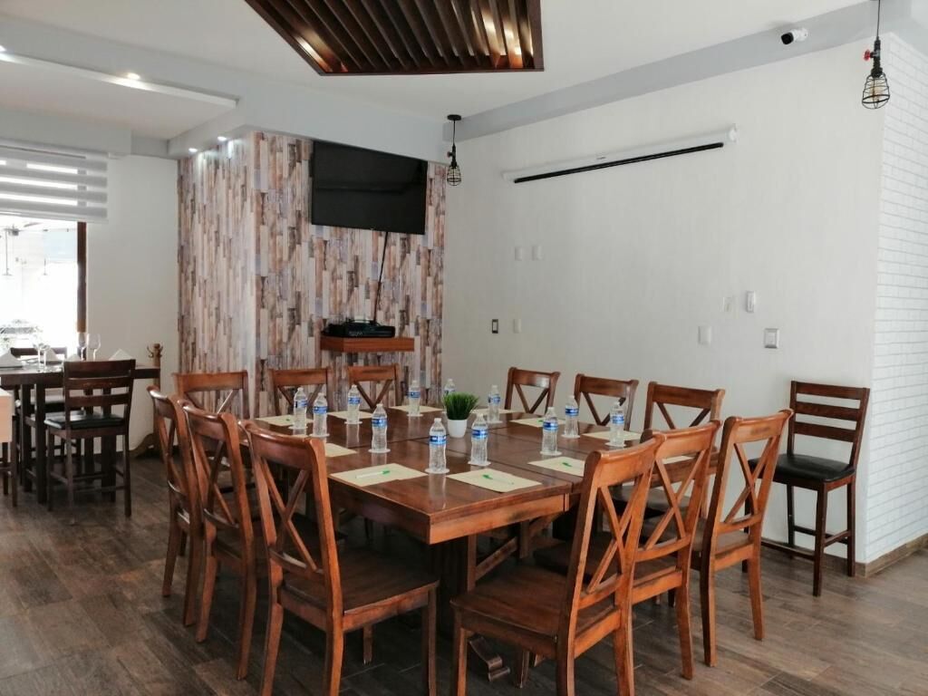 Un comedor con una gran mesa de madera dispuesta para 10 personas, rodeada de sillas de madera. Hay botellas de agua y una pequeña planta en la mesa.