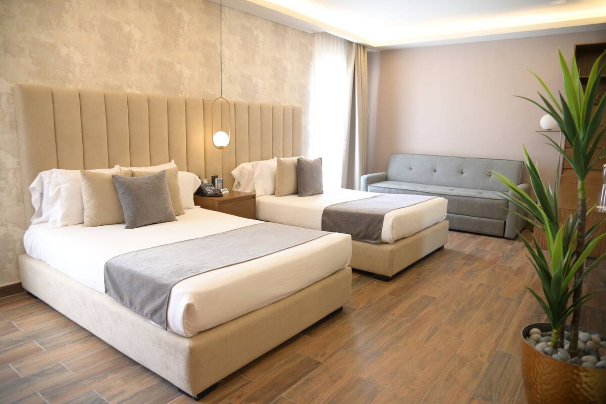 Een hotelkamer met twee bedden, een bank, een nachtkastje met een lamp en een potplant.