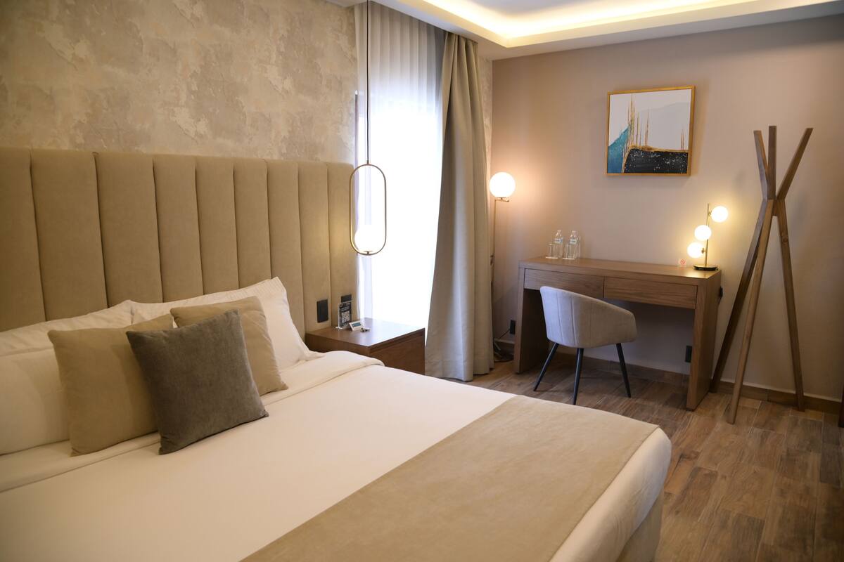 Een hotelkamer met een groot bed, een bureau, een stoel, een lamp en een schilderij aan de muur.