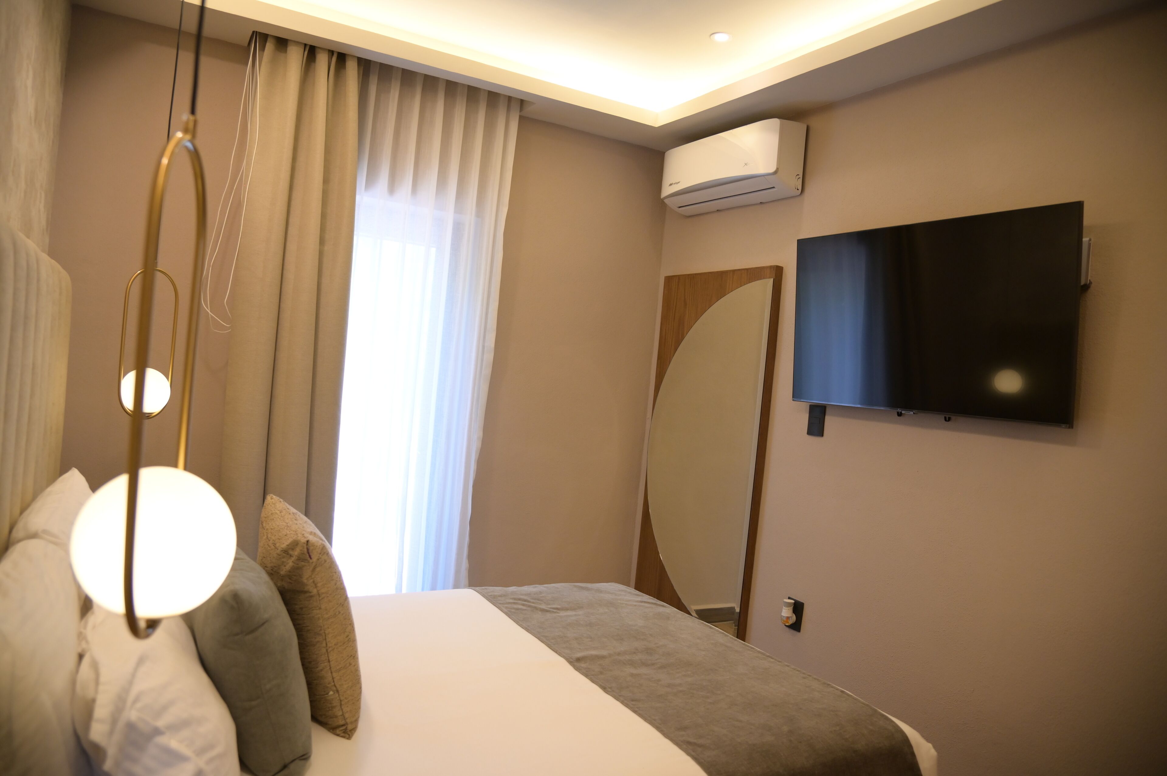 A hotel room with a bed, a TV mounted on the wall, an air conditioning unit, and a window with curtains.