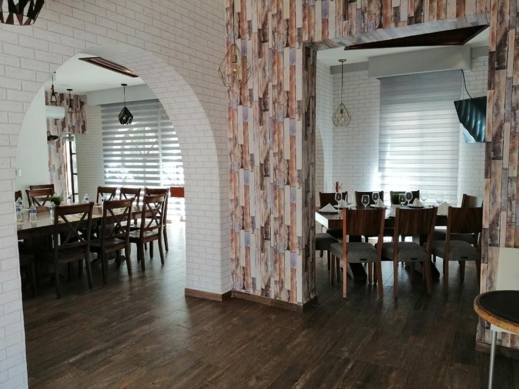A spacious dining area with wooden flooring and a brick wall. There are multiple dining tables and chairs.