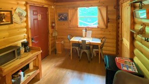 Un accogliente interno di una baita con un tavolo da pranzo in legno, sedie, un angolo caffè e una porta rossa.