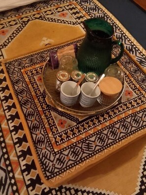 A tray with a green pitcher, two white cups, and a small container on a patterned tablecloth.