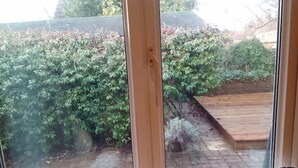 A view through a window with a wooden door frame, a brick pathway, and a wooden deck.