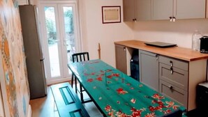 A kitchen with a long table, cabinets, and a refrigerator.