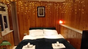A wooden-paneled room with a bed, string lights, and a framed picture on the wall.