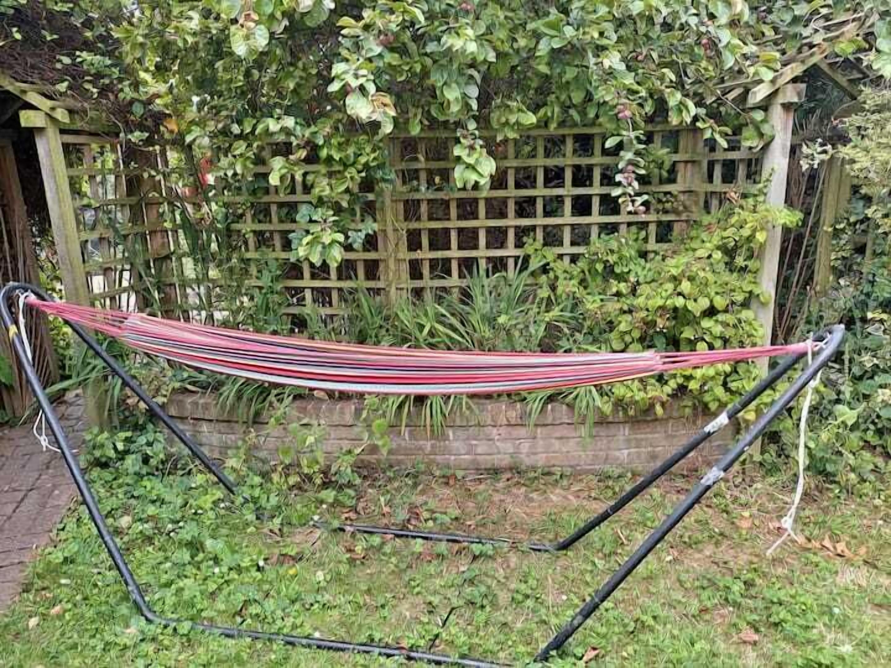 Una hamaca instalada en un jardín con una valla de madera y follaje en el fondo.