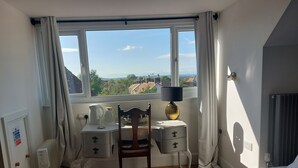 A hotel room with a bed, a desk with a lamp, a chair, a radiator, and a view of the outside. - Pilgrims of the Goddess - Room 8 (Glastonbury)