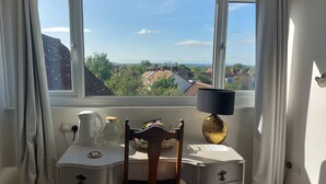 A room with a view of a town through a large window, a desk with a lamp, and a chair. - Pilgrims of the Goddess - Room 8 (Glastonbury)