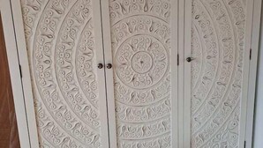 A white wardrobe with intricate floral carvings and three drawers. - Pilgrims of the Goddess - Room 7 (Glastonbury)