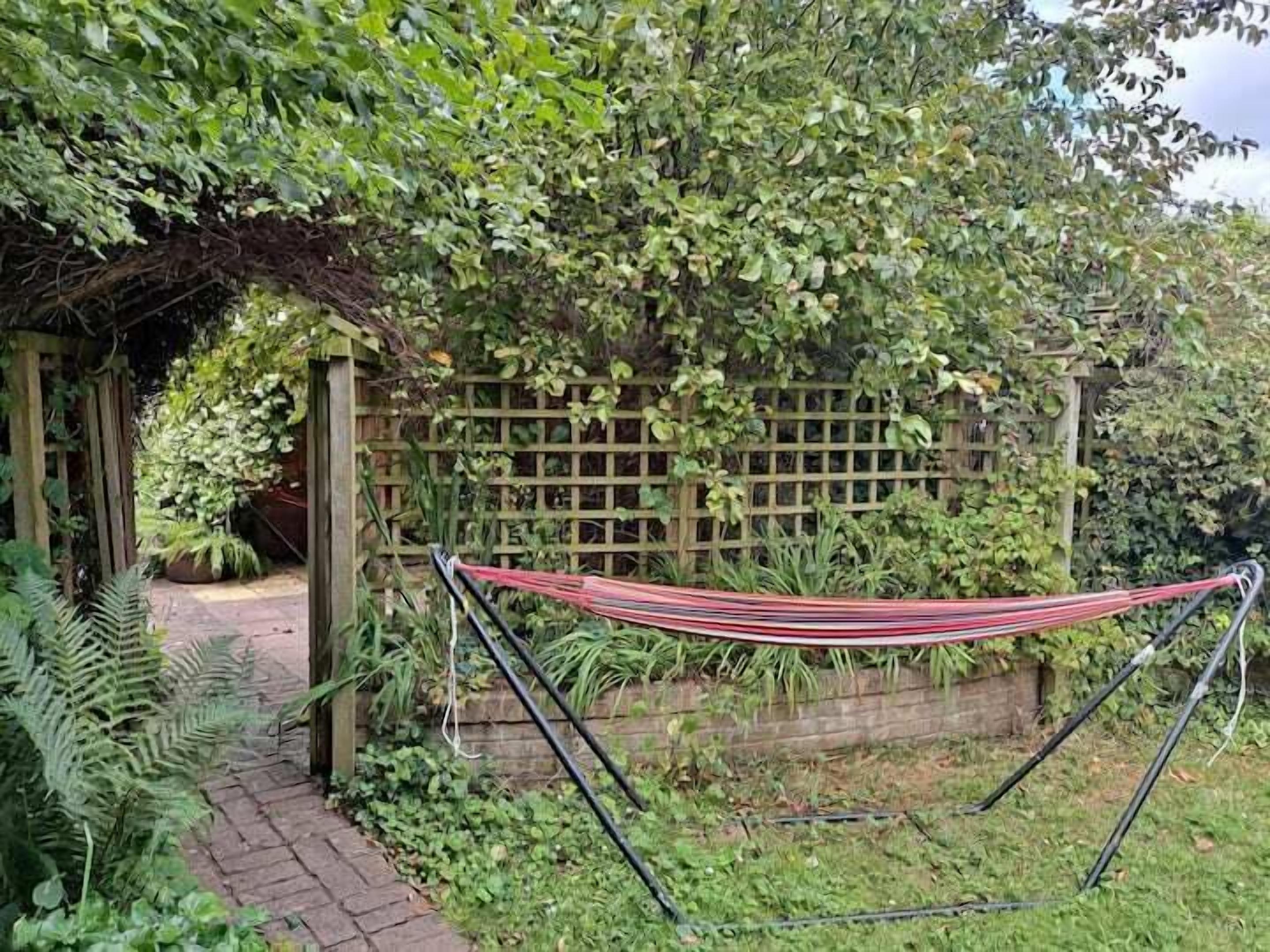 A hammock in a garden with a wooden fence and greenery.