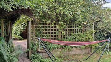 A hammock in a garden with a wooden fence and greenery.