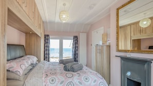 A bedroom with a bed, a mirror, a fireplace, and a view of the sea.
