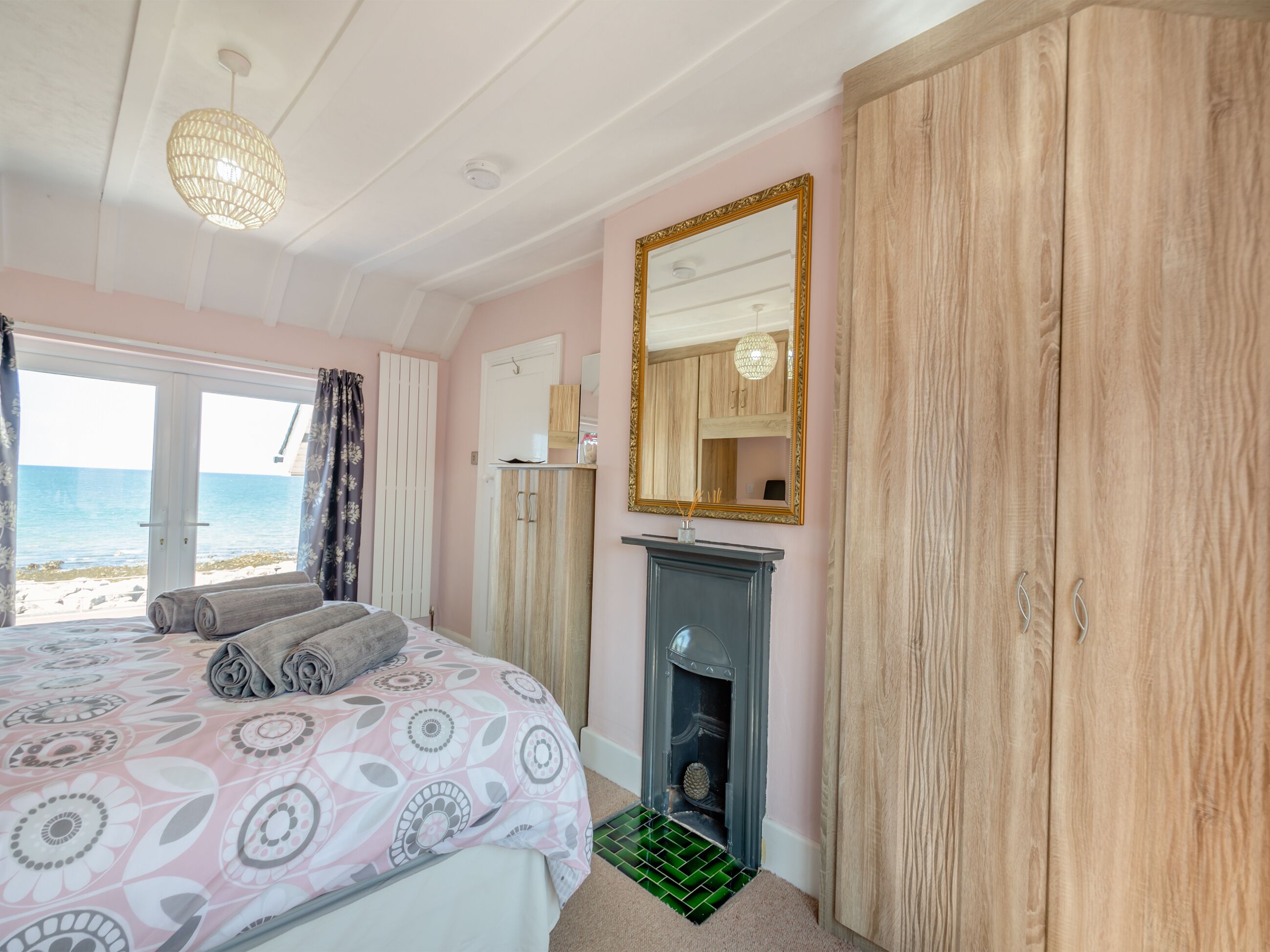 A bedroom with a bed, a mirror, a fireplace, and a view of the sea.