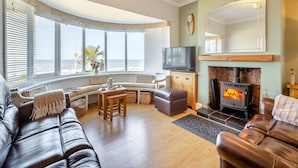 A living room with a fireplace, a television, and a view of the ocean.