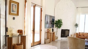 Een moderne woonkamer met een glazen salontafel, een beige fauteuil, een flatscreen-televisie bevestigd aan een witte muur en een open haard.