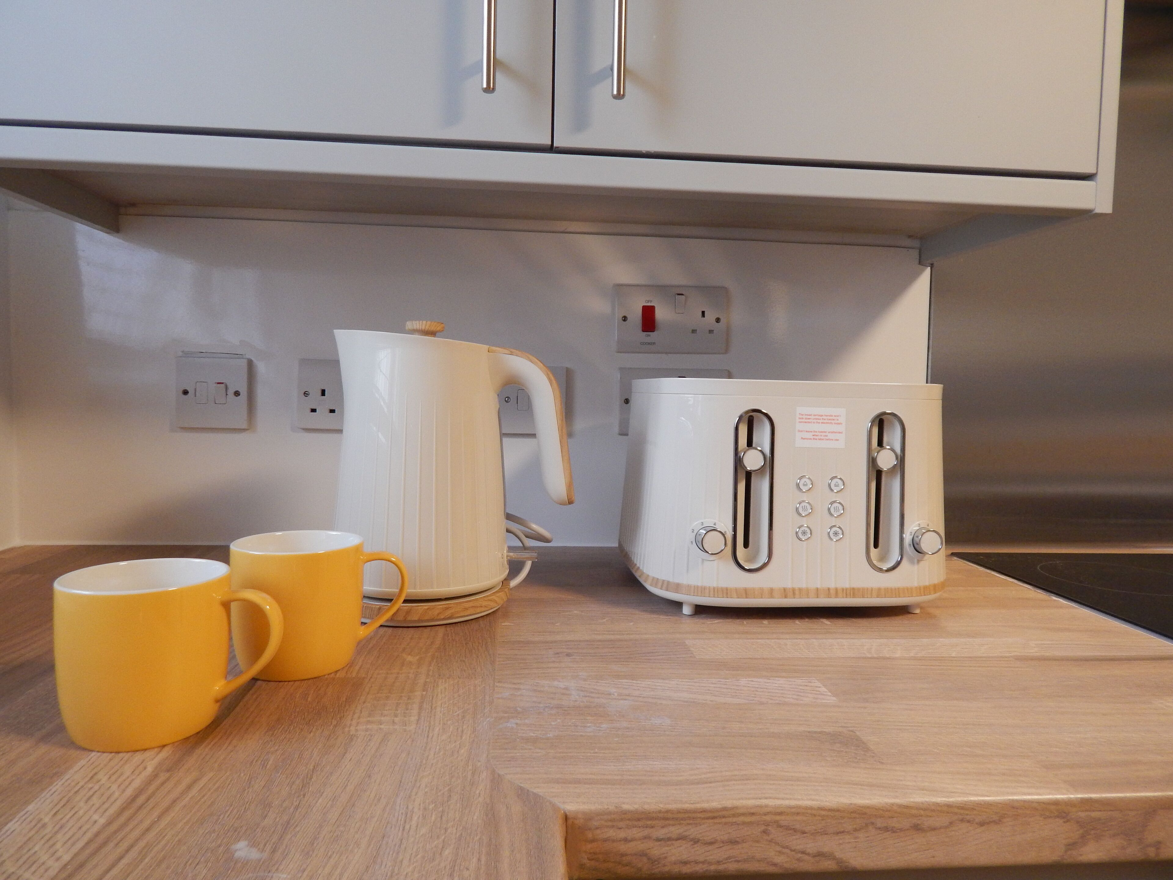 A kitchen counter with a kettle, toaster, and two yellow mugs.