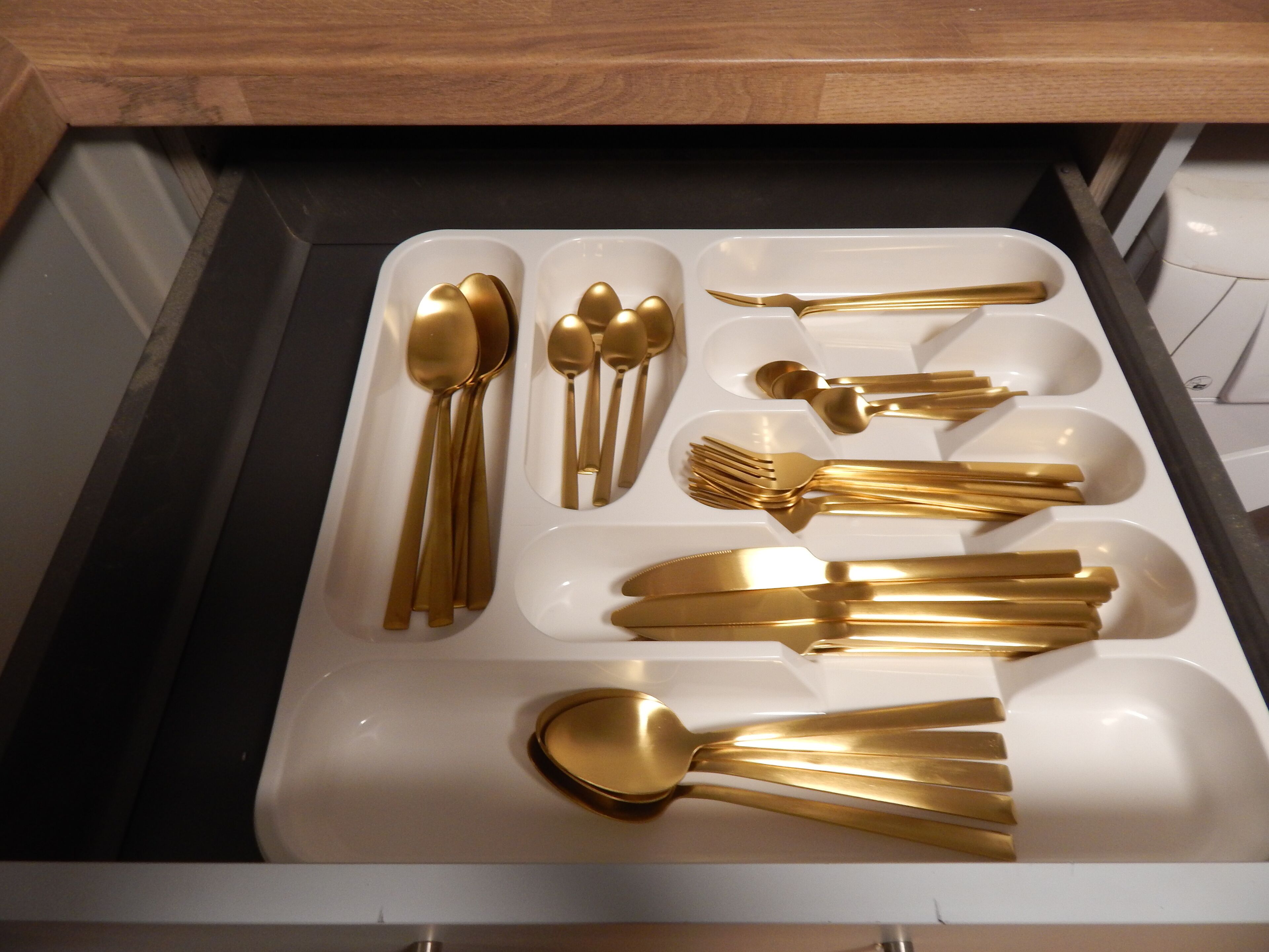 A drawer containing various gold-colored cutlery items including spoons, forks, and knives.