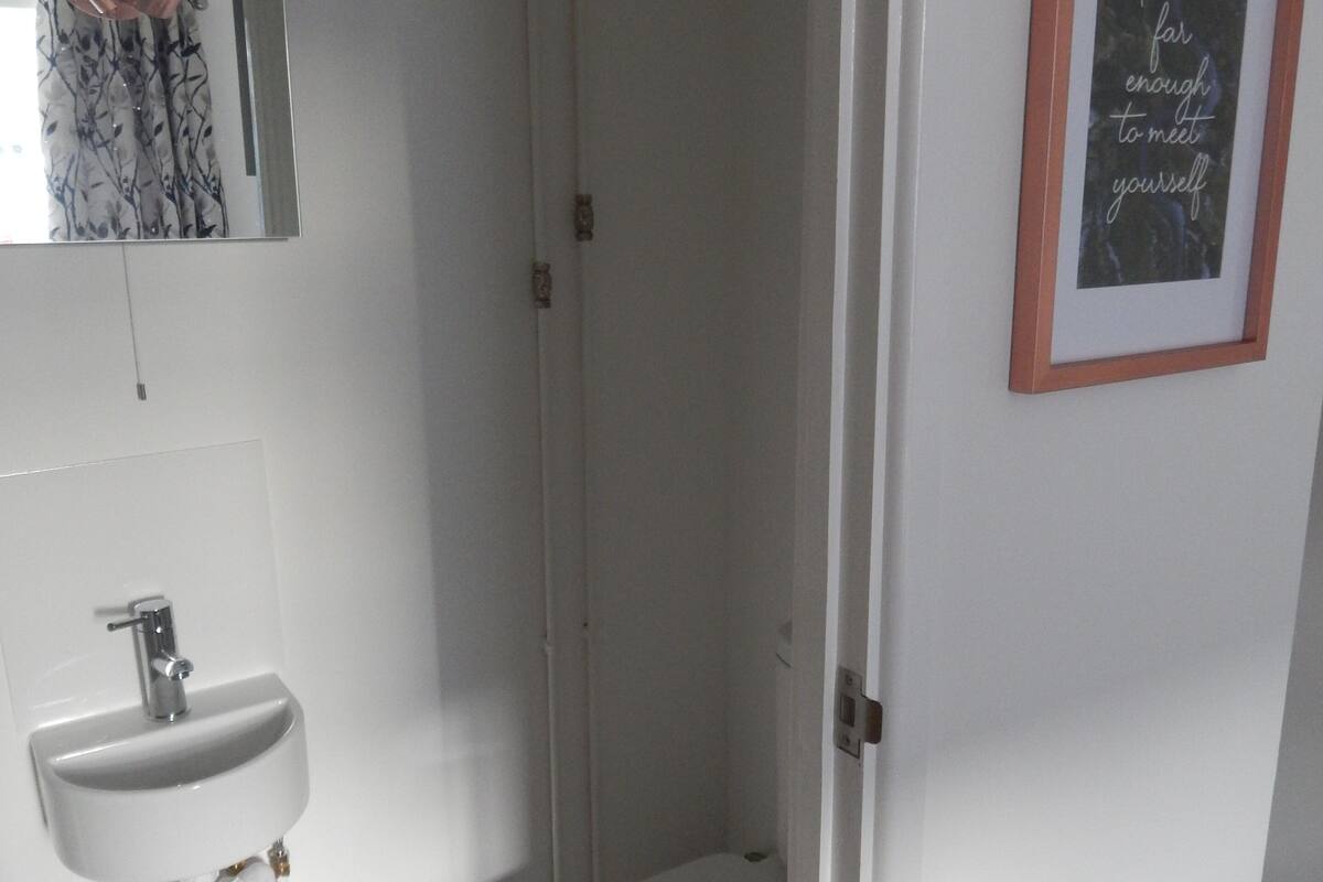 A bathroom with a white sink, toilet, and shower. There is a framed quote on the wall.