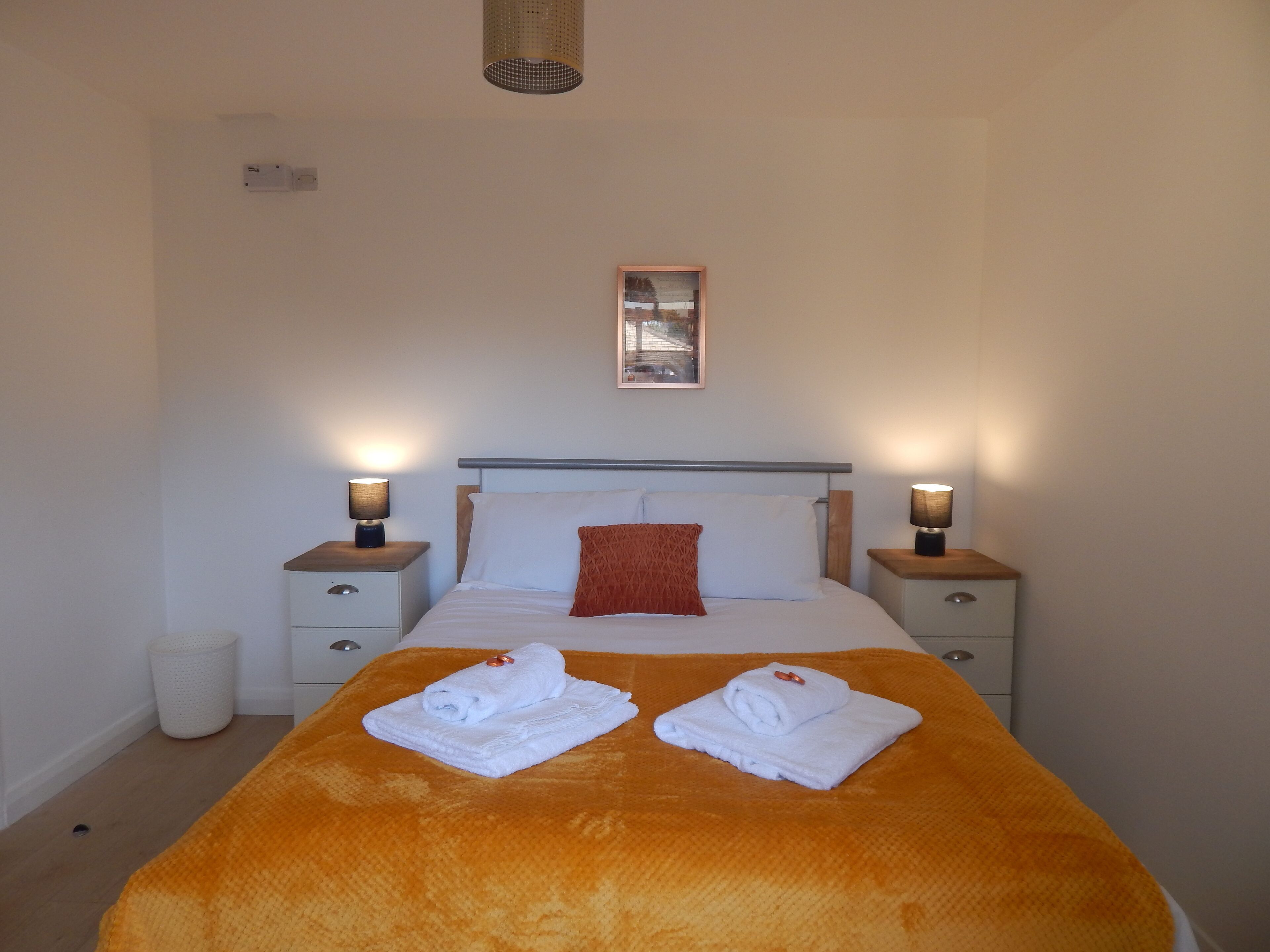 A neatly made bed with two towels, a wooden headboard, and two bedside lamps.