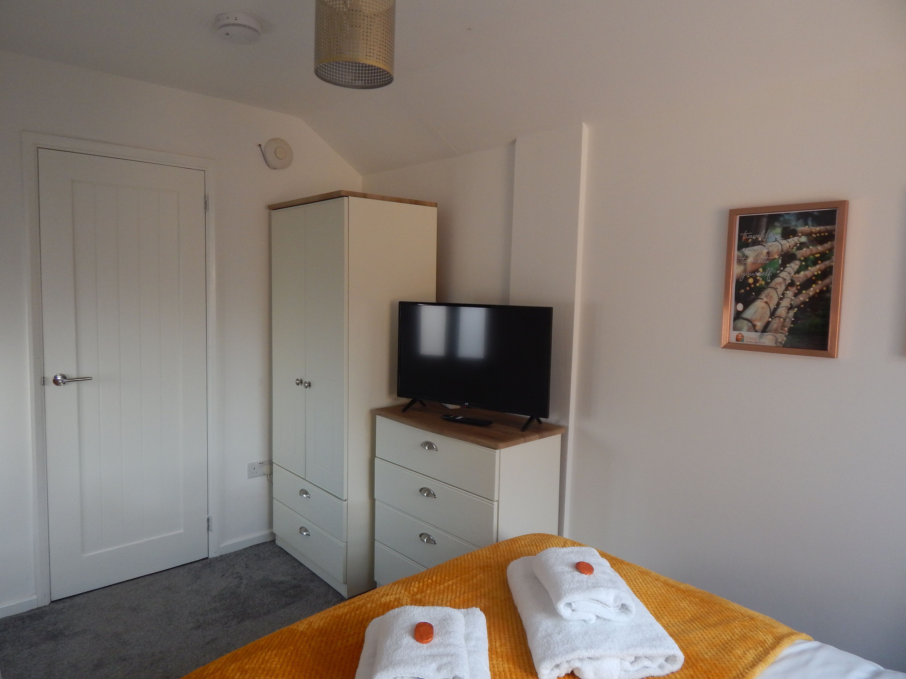 Un dormitorio con cama, televisor sobre un mueble de madera, armario y un cuadro en la pared.