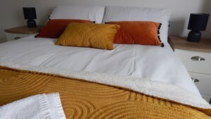 Ein ordentlich bezogenes Bett mit weißer und orangefarbener Bettwäsche, einer gemusterten Tagesdecke und zwei Nachttischen mit Lampen.