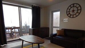 Ein Wohnzimmer mit einer Couch, einem Couchtisch, einem Essbereich mit Stühlen, einem Schrank und einer großen Wanduhr.
