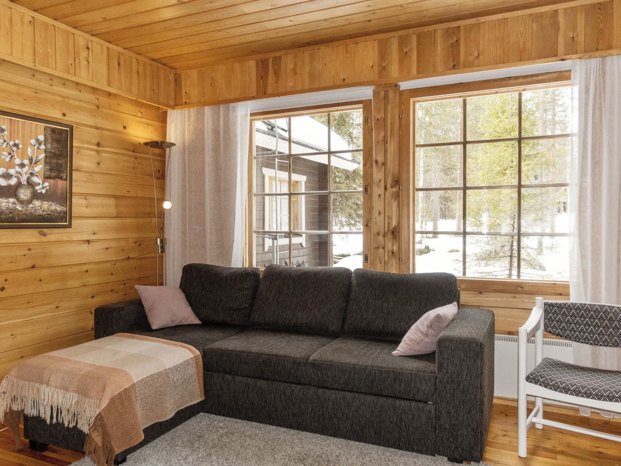 L’intérieur d’un chalet accueillant, avec un canapé gris foncé, une petite table recouverte d’une couverture et un fauteuil agrémenté de coussins à motifs.