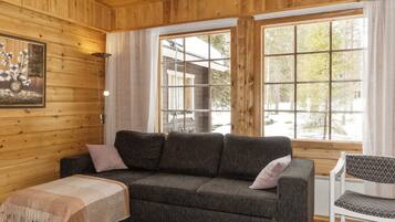 L’intérieur d’un chalet accueillant, avec un canapé gris foncé, une petite table recouverte d’une couverture et un fauteuil agrémenté de coussins à motifs.