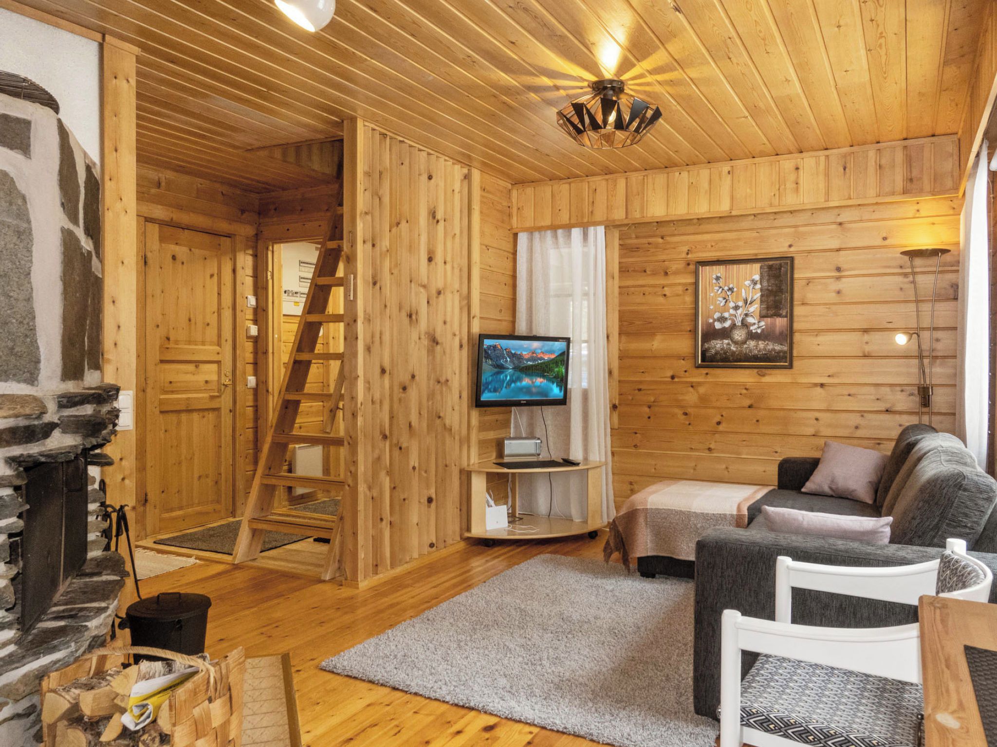 A cozy cabin interior with a fireplace, wooden walls, a television, a sofa, and a ladder.