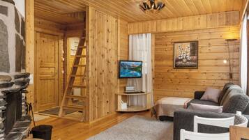 A cozy cabin interior with a fireplace, wooden walls, a television, a sofa, and a ladder.