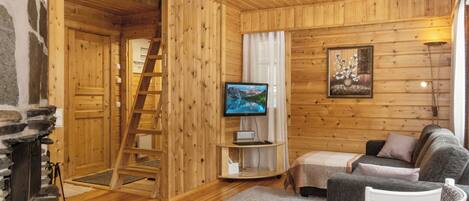 A cozy cabin interior with a fireplace, wooden walls, a television, a sofa, and a ladder.