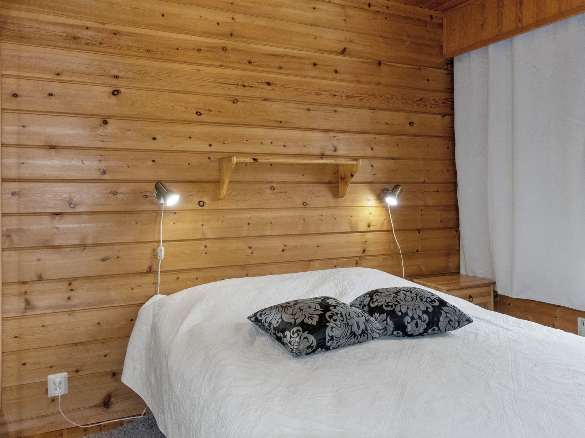 Ein Zimmer mit Holzboden, einem Bett, zwei Nachttischlampen und einer Steckdose an der Wand.
