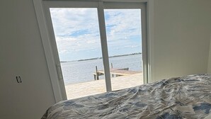 Une chambre avec un grand lit, une vue sur la plage par une porte coulissante et une jetée en bois visible à l’extérieur.
