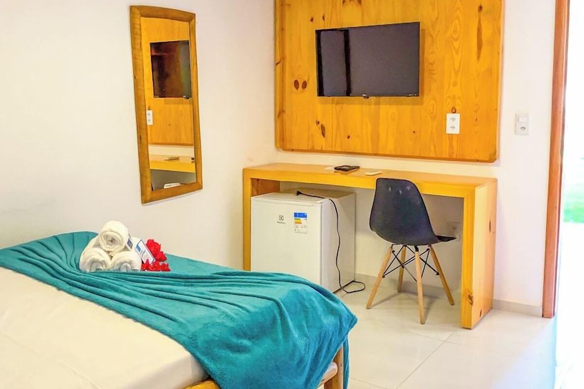 A bedroom with a bed, a desk with a computer, a television, and a small refrigerator.