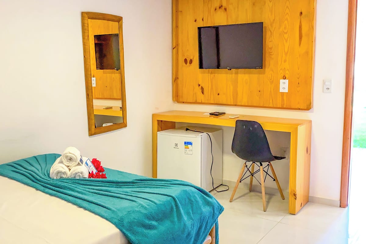 A bedroom with a bed, a desk with a computer, a TV mounted on the wall, and a mirror.