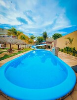 Una piscina con revestimiento azul, rodeada de palmeras y una estructura de techo de paja.