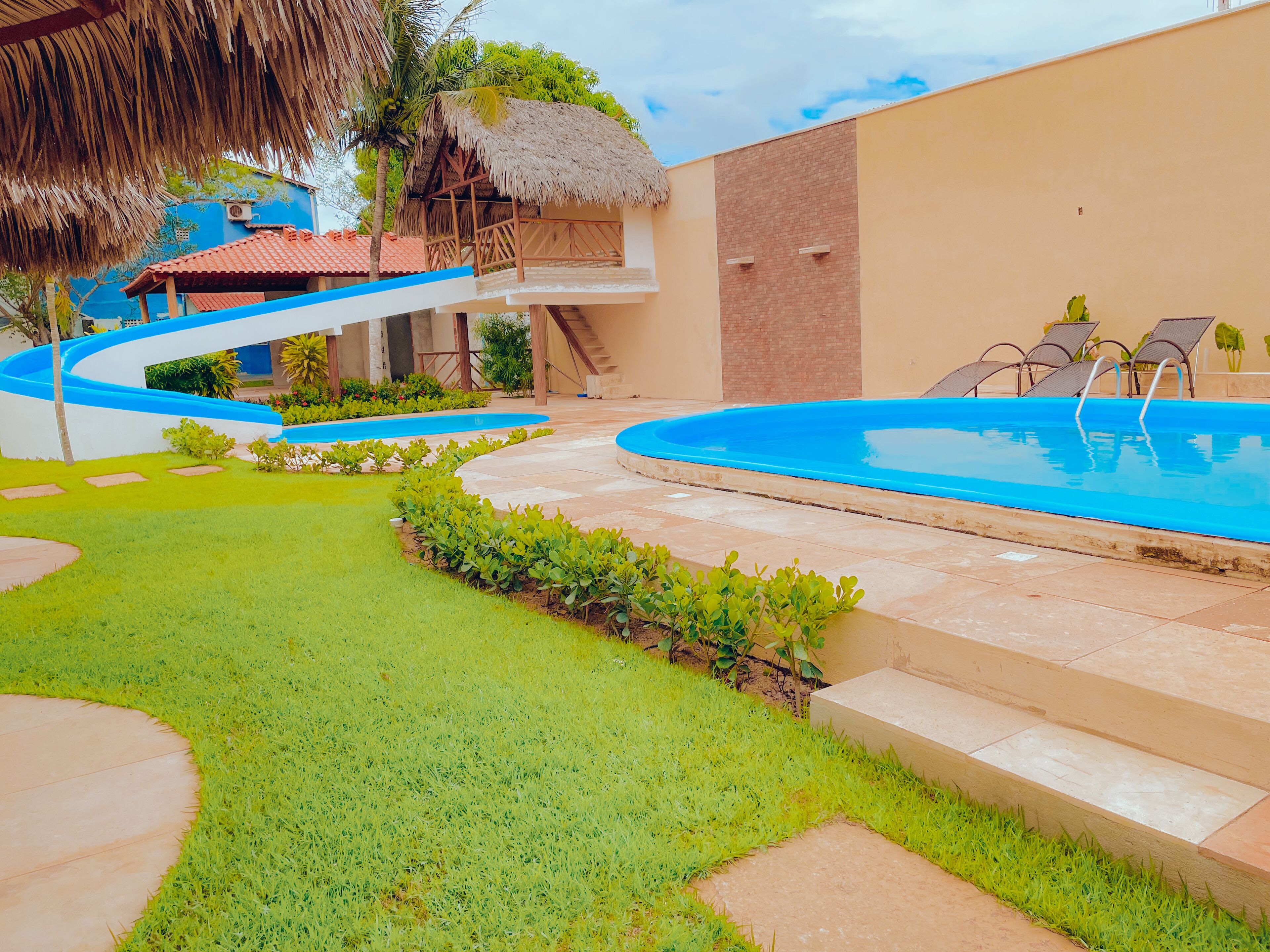 Una piscina con borde azul, una estructura de techo de paja y una escalera que lleva a un segundo nivel.