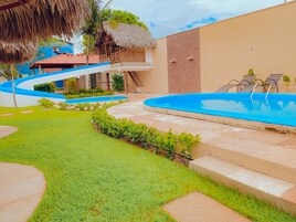 Una piscina con borde azul, una estructura de techo de paja y una escalera que lleva a un segundo nivel.