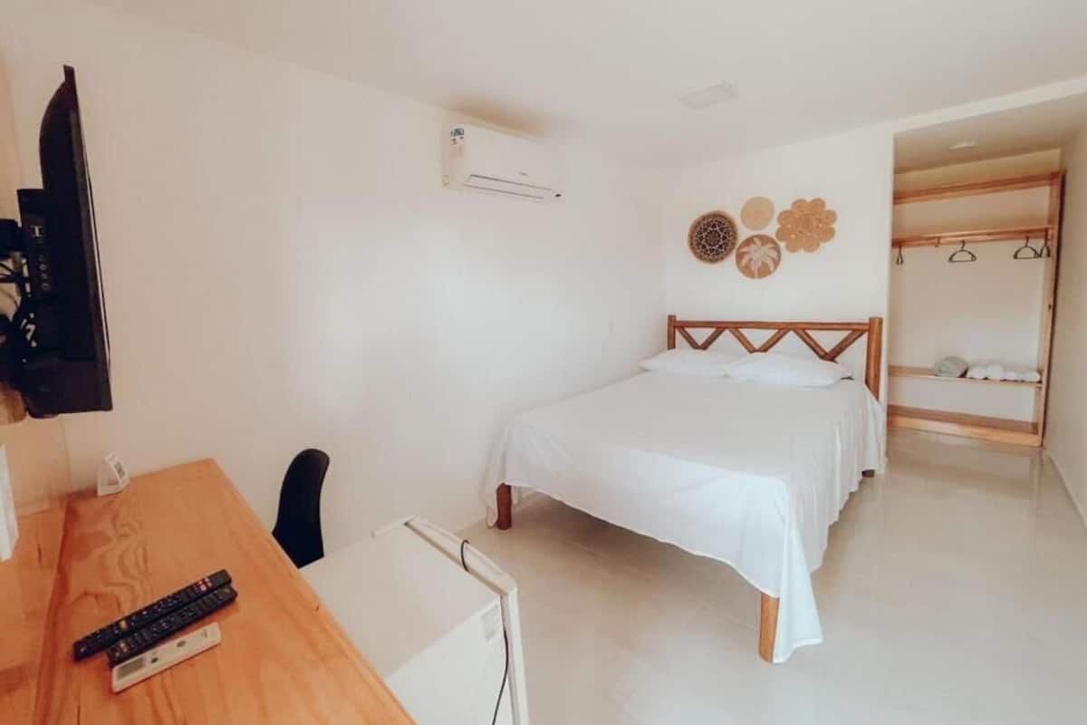 A bedroom with a bed, a desk, a chair, an air conditioning unit, and a wall with decorative items.